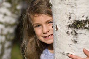 A first grader peeks out from a birch tree during a first grade photo shoot