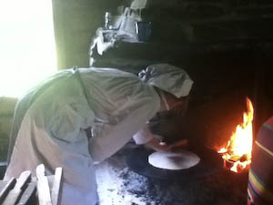 Which is then cooked on an open hearth fire. In this photo a museum employee, dressed like a Norwegian baker of old, checks if it's time to flip the Norwegian flat bread