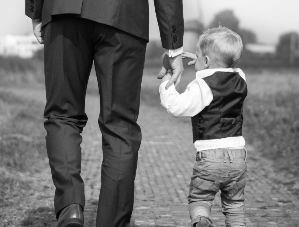 A dapper looking father wearing a suit holds his toddler's hand. It's almost Father's Day. Photo by Sabine van Straaten.