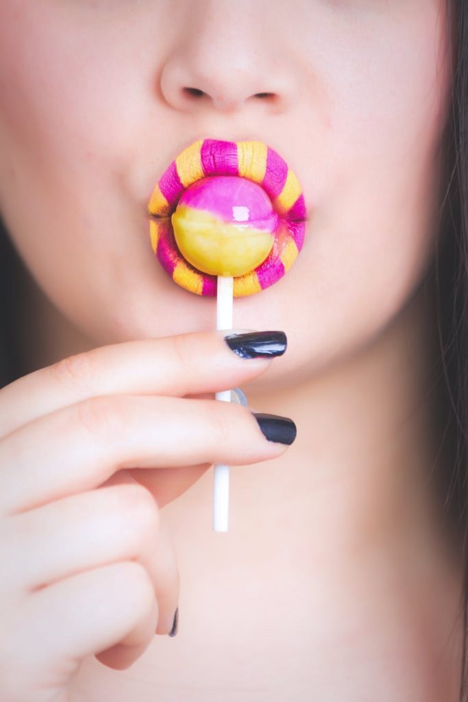 Sugar and Glyphosate: A Tale of Two Toxins. Photo of a woman with yellow and pink lipstick sucking a lolly. Courtesy of Oleg Magni via Pexels. | Jennifer Margulis